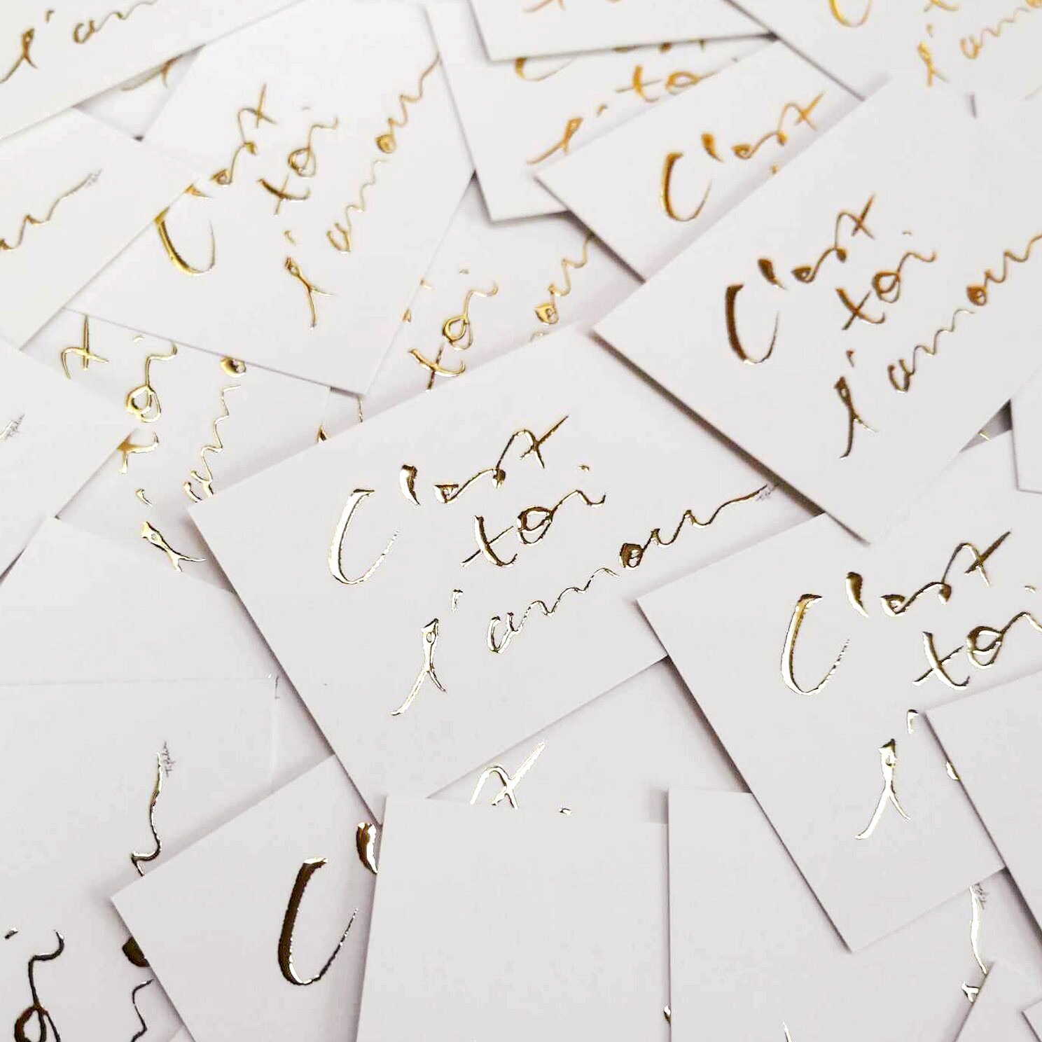 "Mini carte avec inscription dorée C'est toi l'amour, posée sur une pile de cartes similaires"