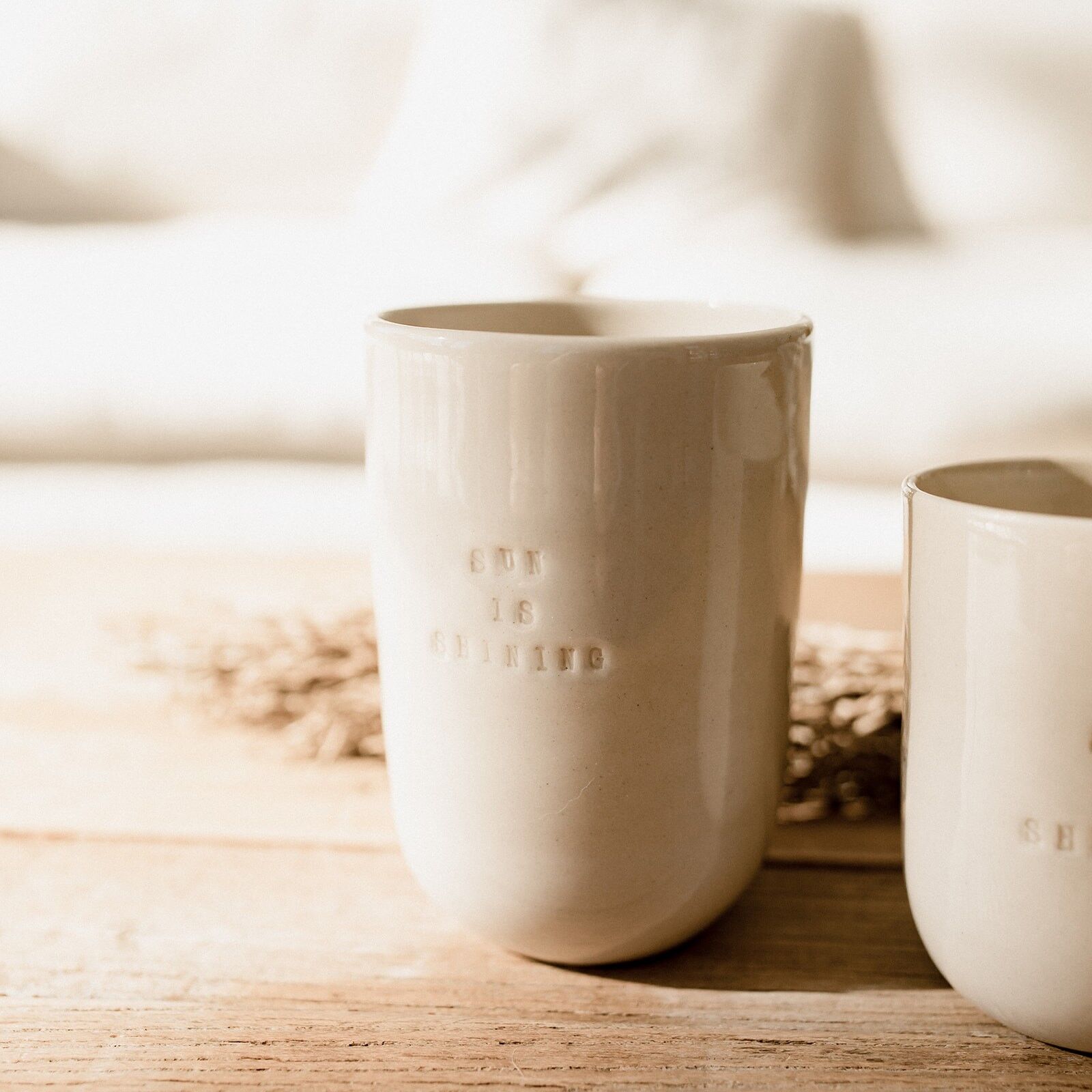 "Tasse artisanale en céramique beige avec inscription Sun is Shining, posée sur une table en bois"