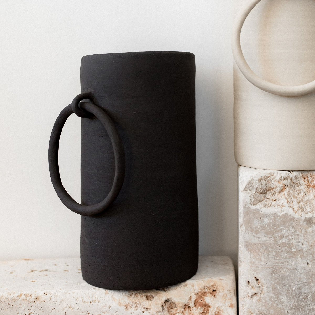 "Vase en céramique noire Big Ring de biais posé sur une pierre brute sur fond blanc"