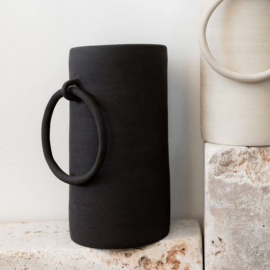 "Vase en céramique noire Big Ring de biais posé sur une pierre brute sur fond blanc"