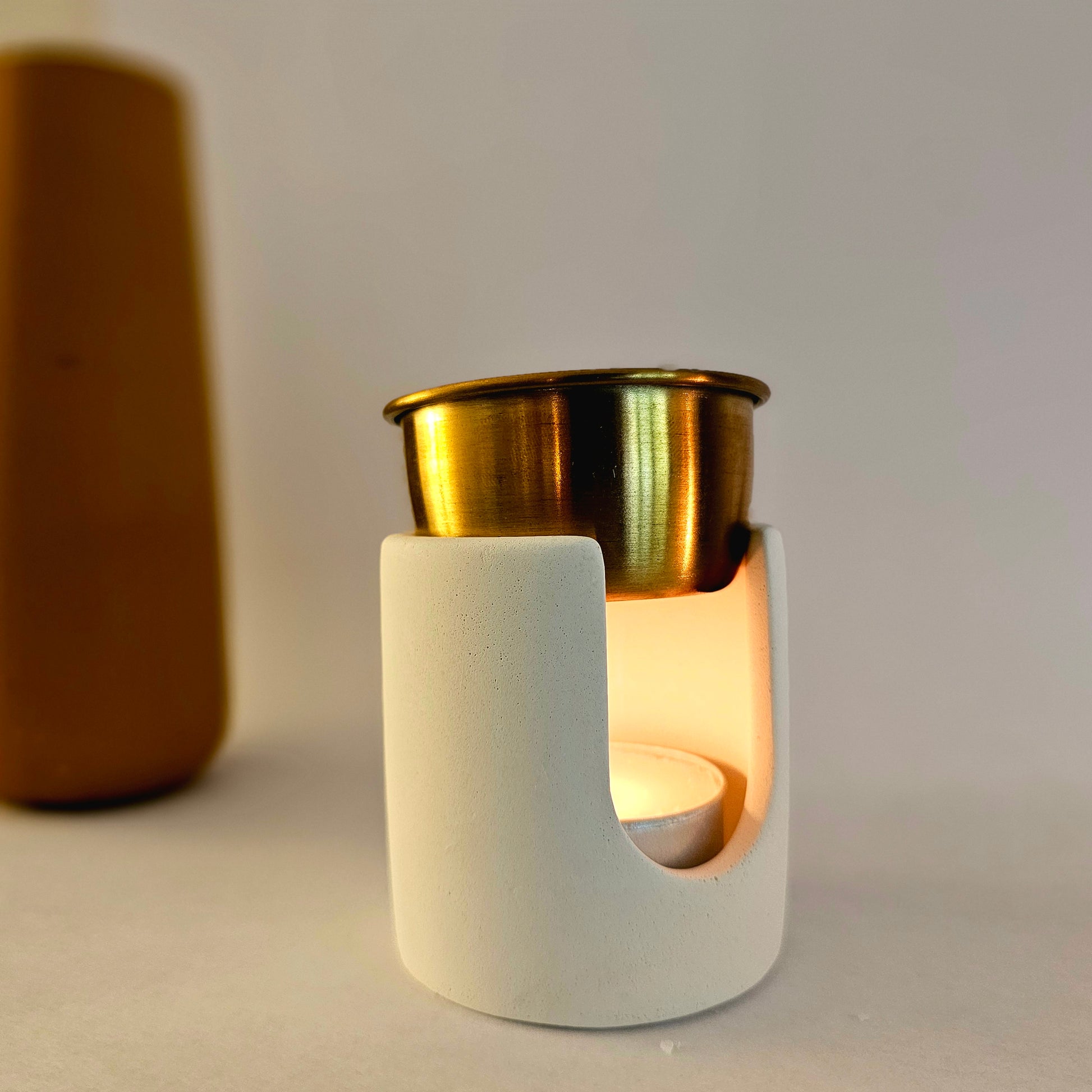 "Brûleur à fondants en béton minimaliste avec un bol en métal doré et une bougie chauffe-plat allumée, posé sur une surface neutre"