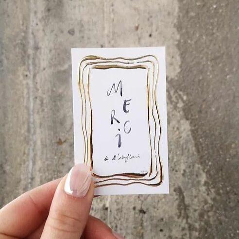 "Mini carte Merci à l'infini avec bordures dorées, tenue par une main, posée sur un fond de béton""