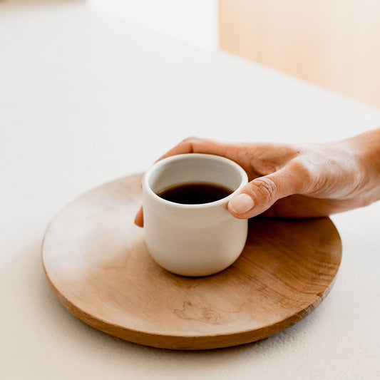 "Tasse à café en céramique naturelle posée sur une assiette en bois, tenue par une main"